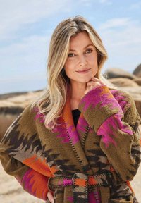 Mehrfarbige, strukturierte Strickjacke in erdigen Tönen mit zickzackartigen Mustern in Rosa, Orange und Grau. Verfügt über eine taillierte Taille und weite Ärmel.