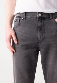 Grå denimjeans med en klassisk femficksdesign, knäppning och en strukturerad yta. Inga synliga logotyper eller mönster.