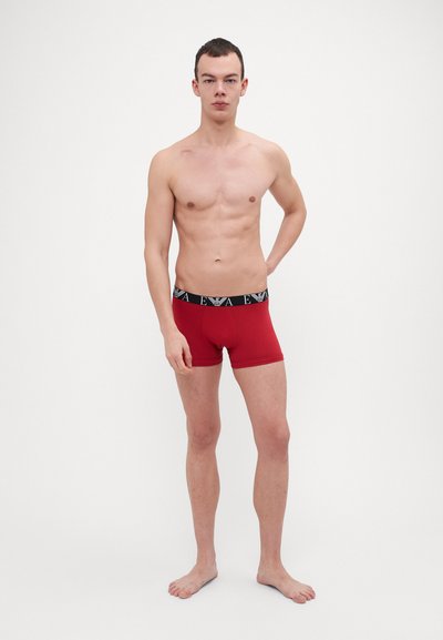 Boxer briefs rossi con una cintura elastica nera che presenta un logo. Il tessuto appare liscio con una vestibilità aderente.