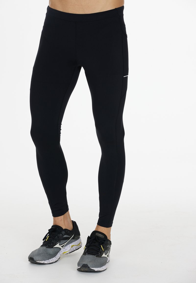 Zwarte leggings van rekbare stof, met een platte tailleband, zijzakken en subtiele stiksels. Gecombineerd met grijze sportschoenen.