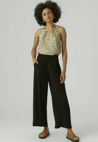 Αμάνικο τοπ με λεοπάρ σχέδιο συνδυασμένο με ψηλόμεσα, φαρδιά μαύρα παντελόνια. Το μοντέλο φοράει καφέ σανδάλια και το ντύσιμο διαθέτει κοψίματα στον λαιμό.