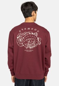 Bordeaux sweatshirt met een witte afbeelding van een slang en de tekst "Creep, Crawl, or Roll" op de achterkant, met geribde manchetten en zoom.