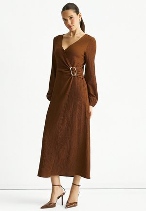 Brown wrap dress with long sleeves, textured fabric, cinched waist featuring a metallic buckle, and ankle-high pointed heels.