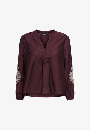 Burgundska bluzica s V-izrezom, dugim rukavima i dekorativnom bijelom vezom na rukavima. Izrađena od teksturirane tkanine s detaljima gumba.