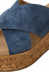 Blauwe suède platform sandaal met kruisbanden, een getextureerde bruine kurken zool en beige accenten. Zichtbare stiksels langs de banden.