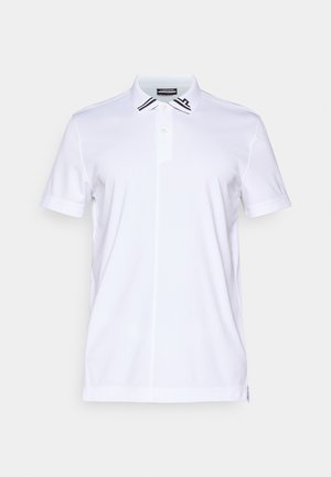 Άσπρη μπλούζα πόλο φτιαγμένη από μαλακό ύφασμα, με κλασικό γιακά, δύο κουμπιά στον λαιμό και μαύρες ρίγες στις άκρες του γιακά.