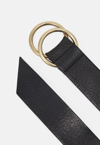 Cinturón de cuero negro texturizado con doble anilla redonda de metal dorado y extremo puntiagudo sobre fondo blanco.