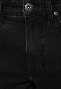 Jeans de mezclilla negra con una textura suave, un diseño clásico de cinco bolsillos y un cierre de botón metálico en la cintura.