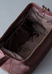 Brown leather bag with a smooth texture. Features a zippered top, spacious interior, and a mesh pocket for organization.