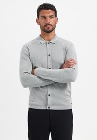 Lichtgrijze gebreide cardigan met een knoopsluiting aan de voorkant, lange mouwen en een kraag. Soepele textuur met donkere knopen als accent.