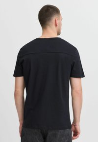Camiseta de manga corta negra con un diseño en el yugo trasero, hecha de una tela suave. Corte recto, estilo minimalista, sin patrones o acentos visibles.