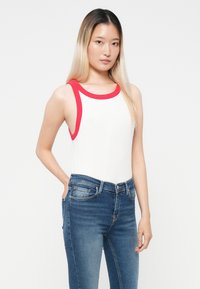 Top blanco sin mangas con acentos rojos, cuello y huecos para los brazos acanalados, combinado con jeans de mezclilla azul que presentan un diseño clásico de cinco bolsillos.