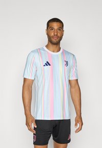 Hellblaues Trikot mit vertikalen Pastellstreifen, ausgestattet mit einem weißen Kragen, schwarzem Adidas-Logo und pinkem Juventus-Wappen. Schwarze Shorts sind inklusive.