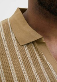 Beige pikétröja med en strukturerad stickad design och vita horisontella ränder, med en platt krage och en avslappnad passform runt halsen.