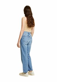 Jeans de cintura alta en azul claro con un ajuste relajado, que cuentan con un diseño de cinco bolsillos y un acabado desgastado, combinados con una camiseta sin mangas beige y zapatillas.