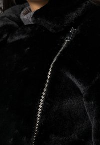Chaqueta de pelaje sintético negro con un diseño elegante, amplio cuello y una cremallera plateada en contraste en la parte delantera para un cierre seguro.