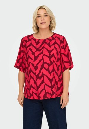 Haut à motifs rouges et roses avec un col rond et des manches courtes, fabriqué en tissu léger, arborant un design zigzag abstrait.