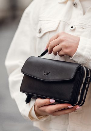 Black leather handbag with a flap closure, zippered edges, and embossed logo on the front. Hand held, featuring a textured finish.