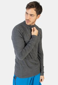 Camiseta deportiva de manga larga gris con cuello alto y media cremallera, que presenta una tela texturizada y un ajuste ceñido, combinada con pantalones cortos azules.