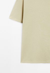 Camicetta beige chiara a maniche corte con una vestibilità comoda, realizzata in morbido cotone, con una texture liscia e cuciture sottili lungo l'orlo.