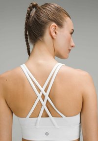 White sports bra with cross-back straps, made of smooth, stretchy fabric. Features a seamless design and a brand logo at the lower back.