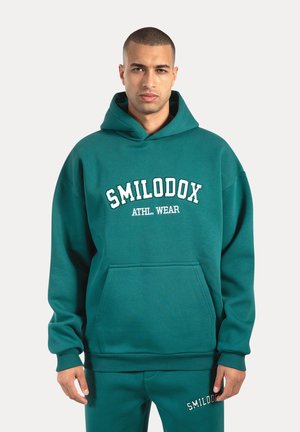 Groene hoodie gemaakt van zacht materiaal, met een kangoeroezak en witte "SMILODOX ATHL. WEAR" tekst over de borst.