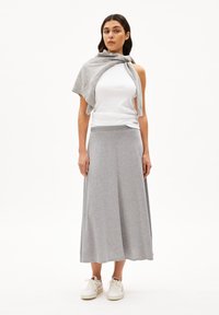 Gray long skirt with a smooth texture, paired with a white tank top. A light gray sweater is draped over shoulders. White sneakers complete the look.