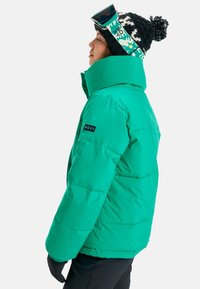Turquoise puffer jacket with a high collar, featuring a Roxy logo on the sleeve. Paired with a black and patterned knit beanie.