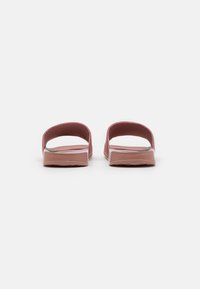 Pink slide sandals with open backs, flat rubber soles, and minimalistic design. Curved straps provide a simple, unobtrusive look.
