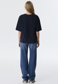 Donkerblauwe oversized t-shirt met korte mouwen, gecombineerd met lichtblauwe wijde jeans. De stof lijkt soepel en heeft een ontspannen pasvorm.