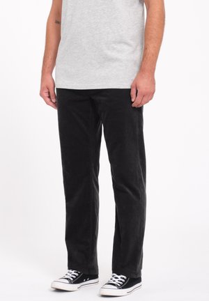 Zwarte corduroybroek met een recht model, voorzien van subtiele ribbels, gecombineerd met zwart-witte canvas sneakers.
