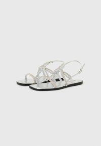Silver sandals with intricate straps and rhinestone accents, flat black sole, open toe design, and adjustable ankle strap.