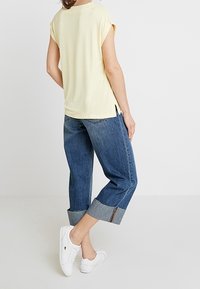 Gul kortærmet T-shirt, afslappet pasform, parret med brede blå jeans med opsmøg; hvide sneakers fuldender outfittet.