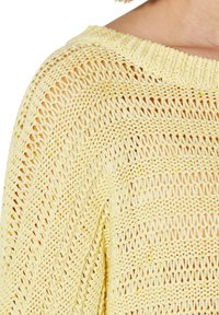 Hellgelber Strickpullover mit offener Maschenführung, weitem Ausschnitt und lässiger Passform, der ein strukturiertes, luftiges Design zeigt.