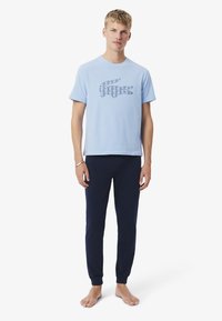 T-shirt en coton bleu clair avec un logo crocodile géométrique bleu marine, accompagné d'un pantalon de jogging bleu marine avec des poignets effilés.