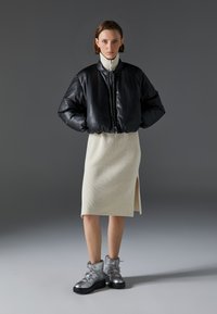 Chaqueta bomber de cuero negro con cierre de cremallera, falda de punto crema hasta la rodilla y botas de tobillo plateadas con suelas gruesas y cordones.