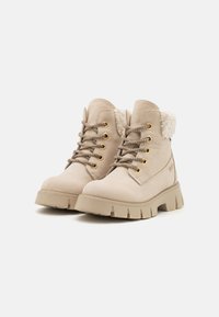 Beige faux skinnankler støvler med en fluffy krage, gullfargede snorer og en robust, chunky såle for holdbarhet og grep.