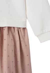 Weißes Sweatshirt mit geripptem Saum über einem rosa Rock mit kleinen, glänzenden Herzmustern, aus weichem, strukturiertem Stoff.