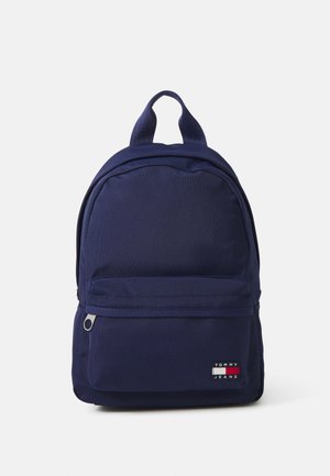 Mochila de tela azul marino con un compartimento principal y un bolsillo frontal con cremallera; cuenta con un parche con logo y doble asa en la parte superior para un fácil transporte.