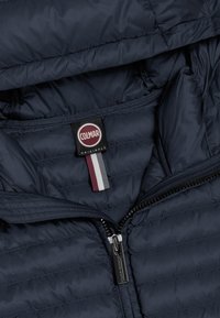 Navy puffer jacket interior featuring a Colmar label with a red logo and a striped accent. Smooth, quilted texture, zip closure detail.