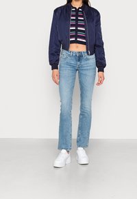 Chaqueta de bombardero azul marino, top de punto cropped a rayas, jeans acampanados de tono azul claro y zapatillas blancas de plataforma. Textura suave y diseño ajustado.