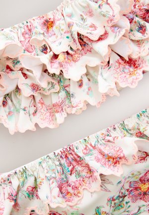 Tela floral con volante en blanco con patrones en rosa y verde. Cuenta con bordes con ondas y una banda elástica para mayor flexibilidad.