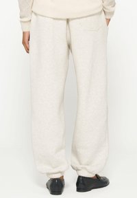 Lichtbeige fleece joggingbroek met elastische manchetten, zijzakken en een subtiele textuur. Draagt met zwarte loafers.