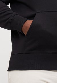 Black sweatshirt with ribbed cuffs and hem, featuring a front pocket. The material is soft and textured, suitable for casual wear.