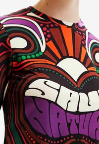 Barevná vzorovaná košile s kulatým výstřihem, zdobená výraznými víry a tečkami v oranžové, zelené, fialové a hnědé barvě na tmavém pozadí.