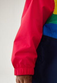 Spalvota daugialypė striukė su raudonomis, geltonomis, žaliosiomis, mėlynomis ir tamsiai mėlynomis dalimis. Turinti elastinius rankogalius ir lygų paviršių.
