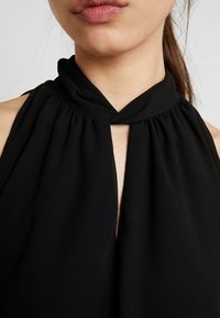 Top nero senza maniche con scollatura annodata, design a occhiello sul davanti e delicate pieghe. Realizzato in tessuto leggero.