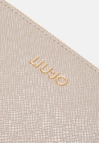 Beige texturovaná peněženka se zipovým uzavřením, se zlatým logem "LIU JO" a jemným prošíváním podél okraje pro přidaný detail.