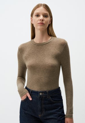 Long-sleeve, fitted top in light brown fabric, featuring a round neckline. Paired with dark blue high-waisted jeans with pockets.