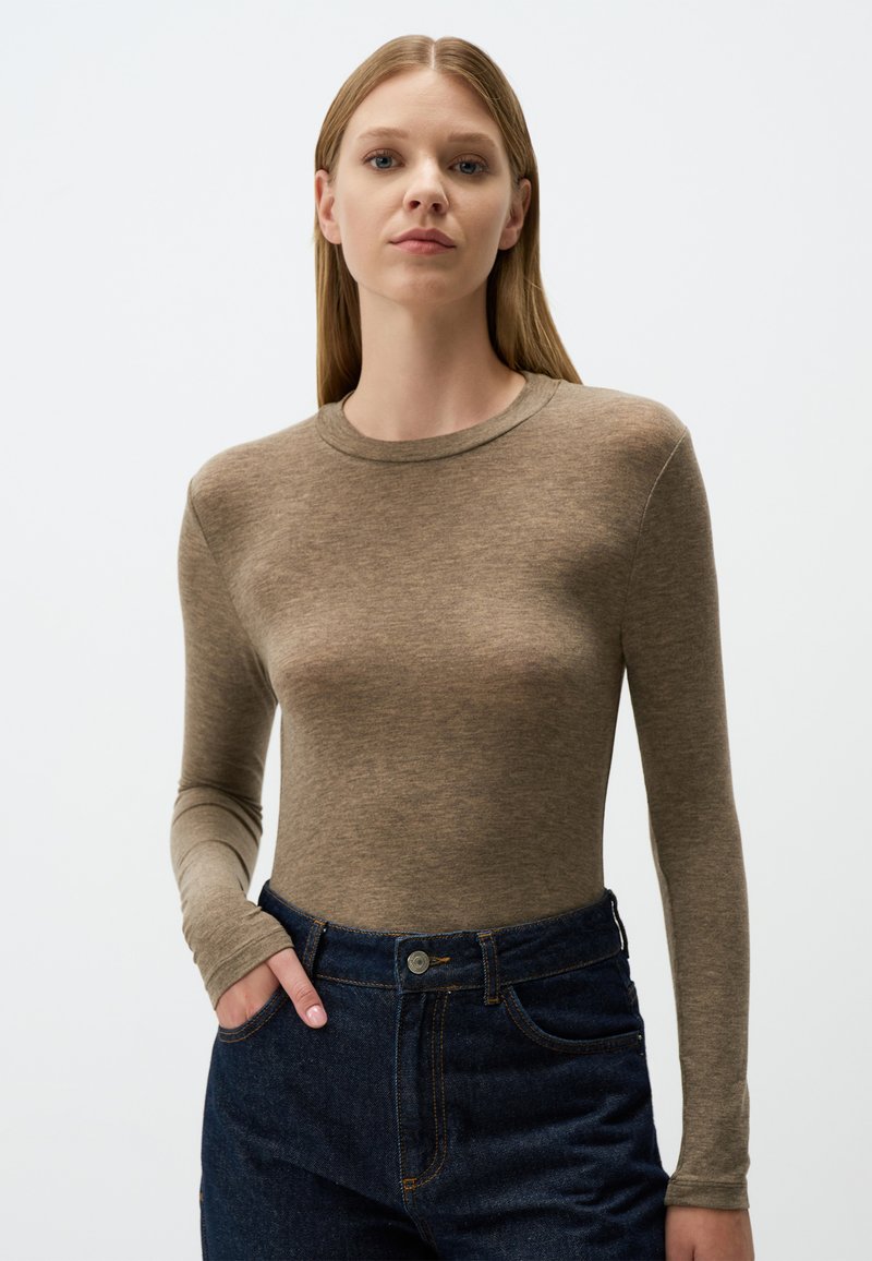 Top a maniche lunghe aderente in tessuto marrone chiaro, con scollatura tonda. Abbinato a jeans a vita alta blu scuro con tasche.